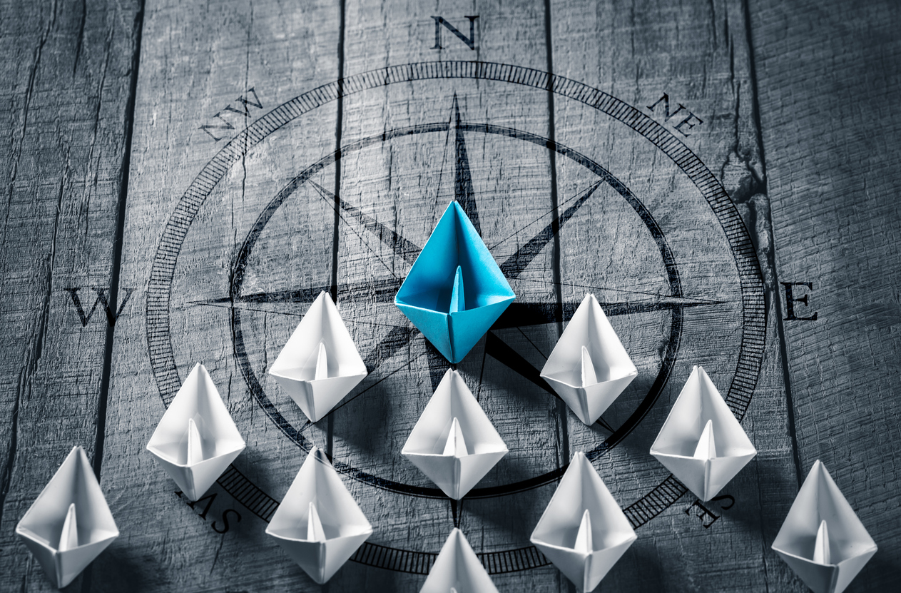 Blue Paper Boat Leading A Fleet Of Small White Boats With Compass Icon On Wooden Table - Leadership Concept- representing-executive coaching to move your forward
